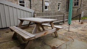 Une table de pique-nique en bois, avec des bancs, installée sur une terrasse en pierre.