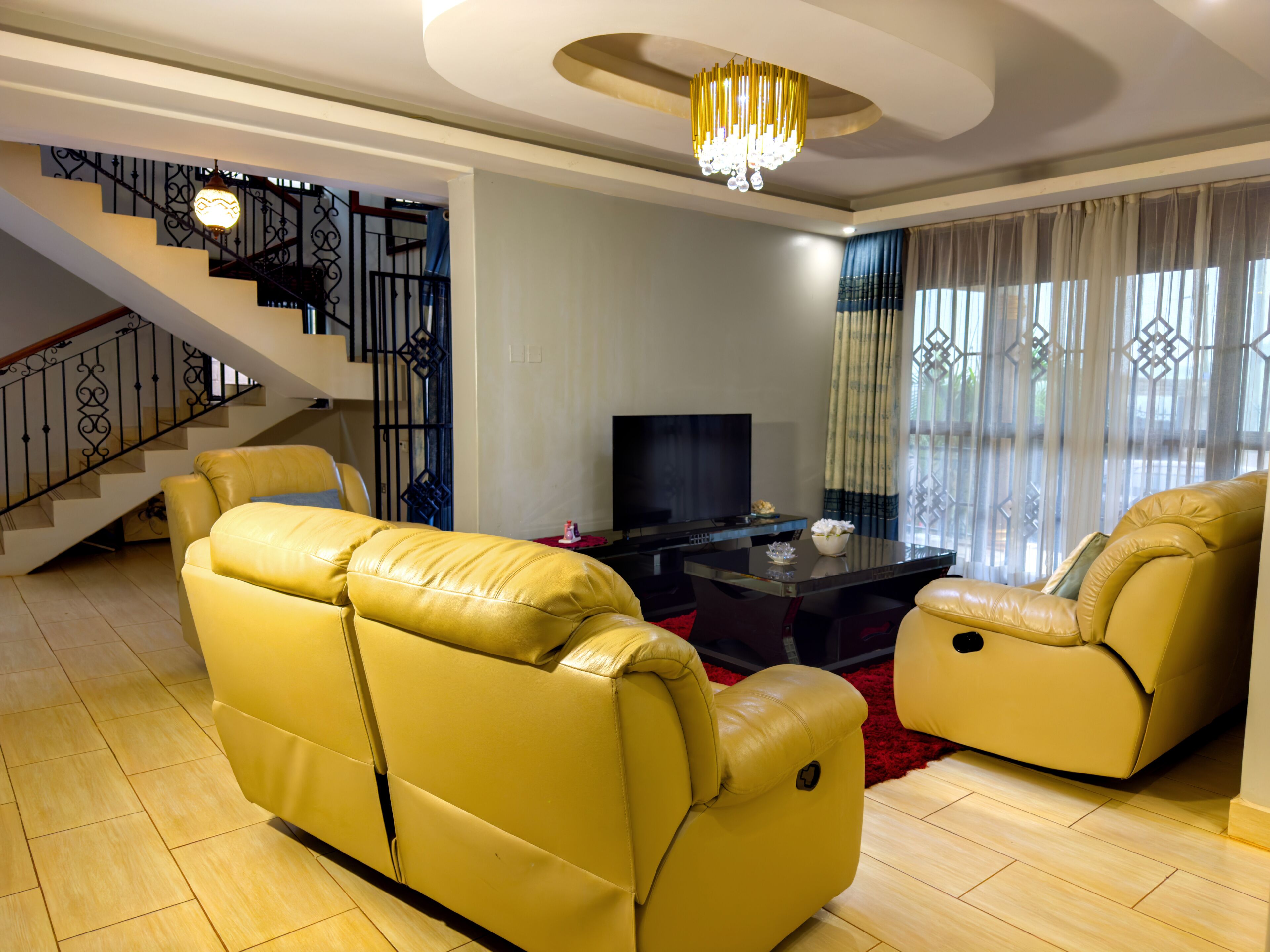 Un soggiorno con una scala, divani in pelle, una TV a schermo piatto e un lampadario.