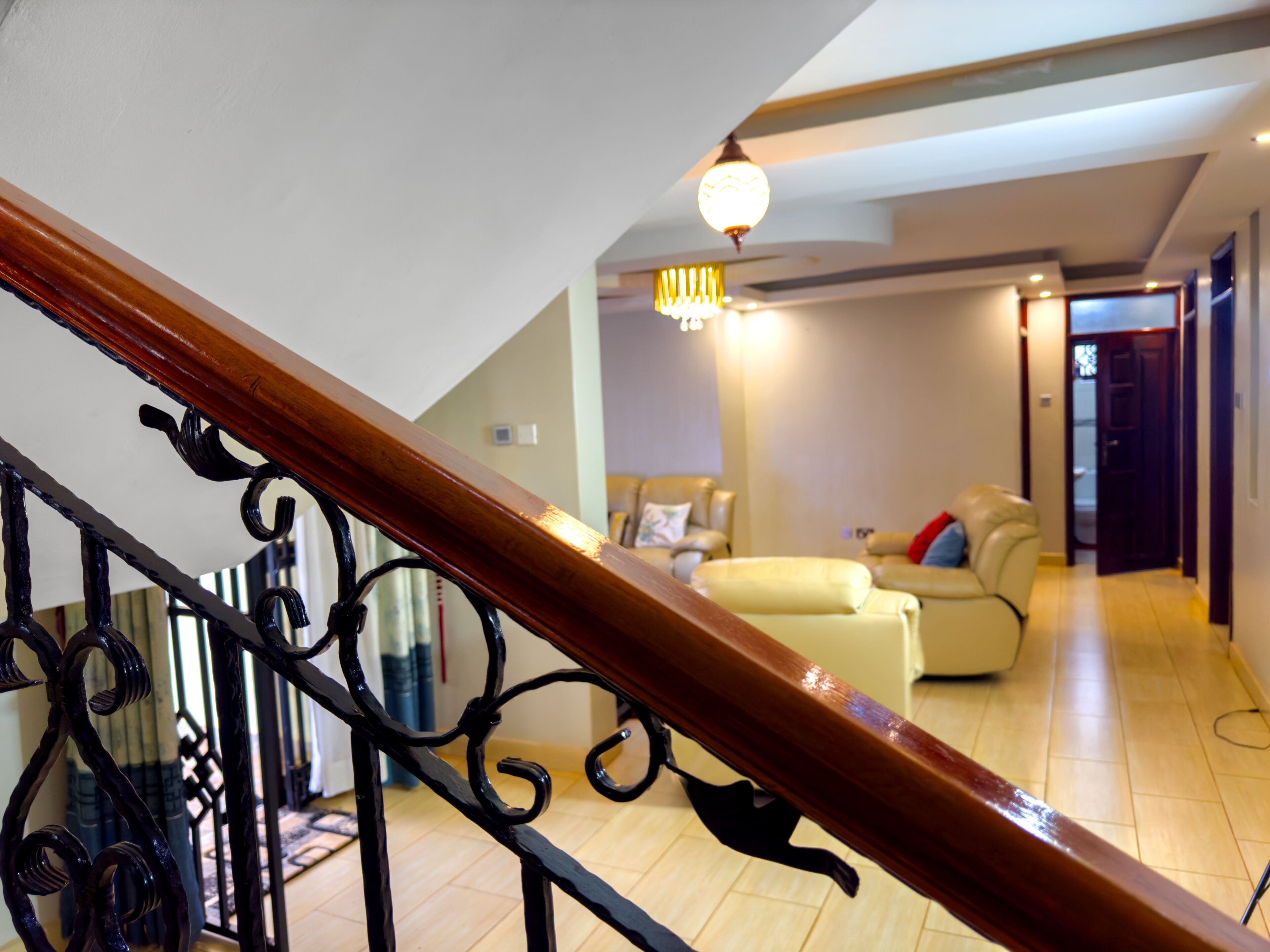Eine Treppe mit hölzernem Geländer und schwarzen Metallspindeln, die in ein Wohnzimmer mit Sofa und einer Deckenleuchte führt.