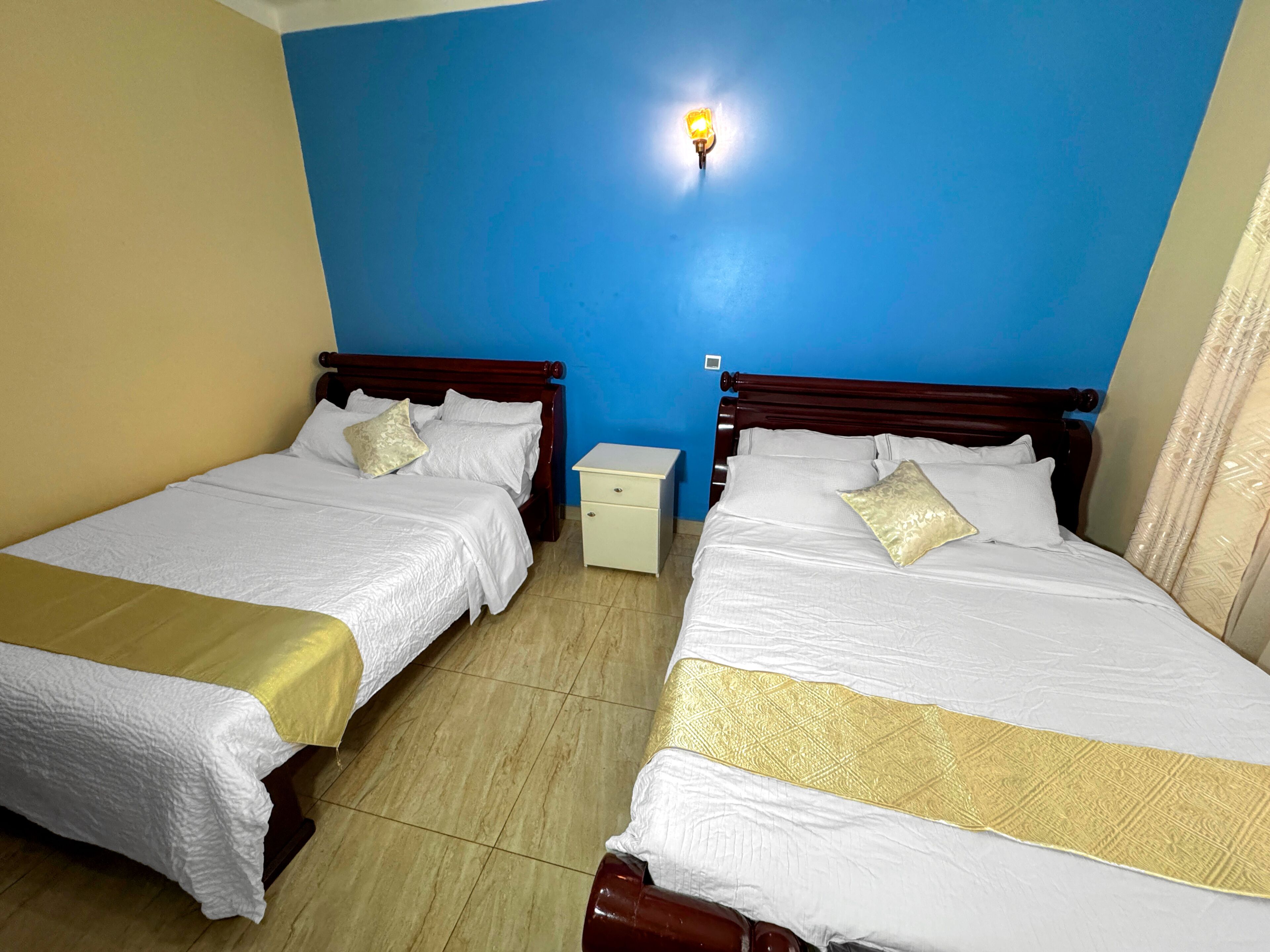A hotel room with two single beds, a nightstand, and a wall-mounted light fixture.