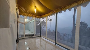 Una habitación con piso de baldosas, un ventanal con vistas a árboles y una cerca, y una lámpara colgante.