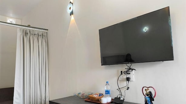 Una habitación con un televisor de pantalla plana montado en la pared, un mueble de madera oscura con una cesta y una botella de agua encima, y una estatua decorativa.