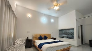 Un dormitorio con cama, ventilador de techo, mesita de noche, una silla y una ventana.