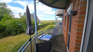 En balkong med ett bord och stolar, ett hängande parasoll och utsikt över havet.
