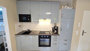 A compact kitchen with a microwave, oven, and coffee maker, featuring white cabinets and a tiled backsplash. - Fantastic vacation rental "FeWo Lieblingsplatz" right on the beach in California O (Schönberg (Holstein))