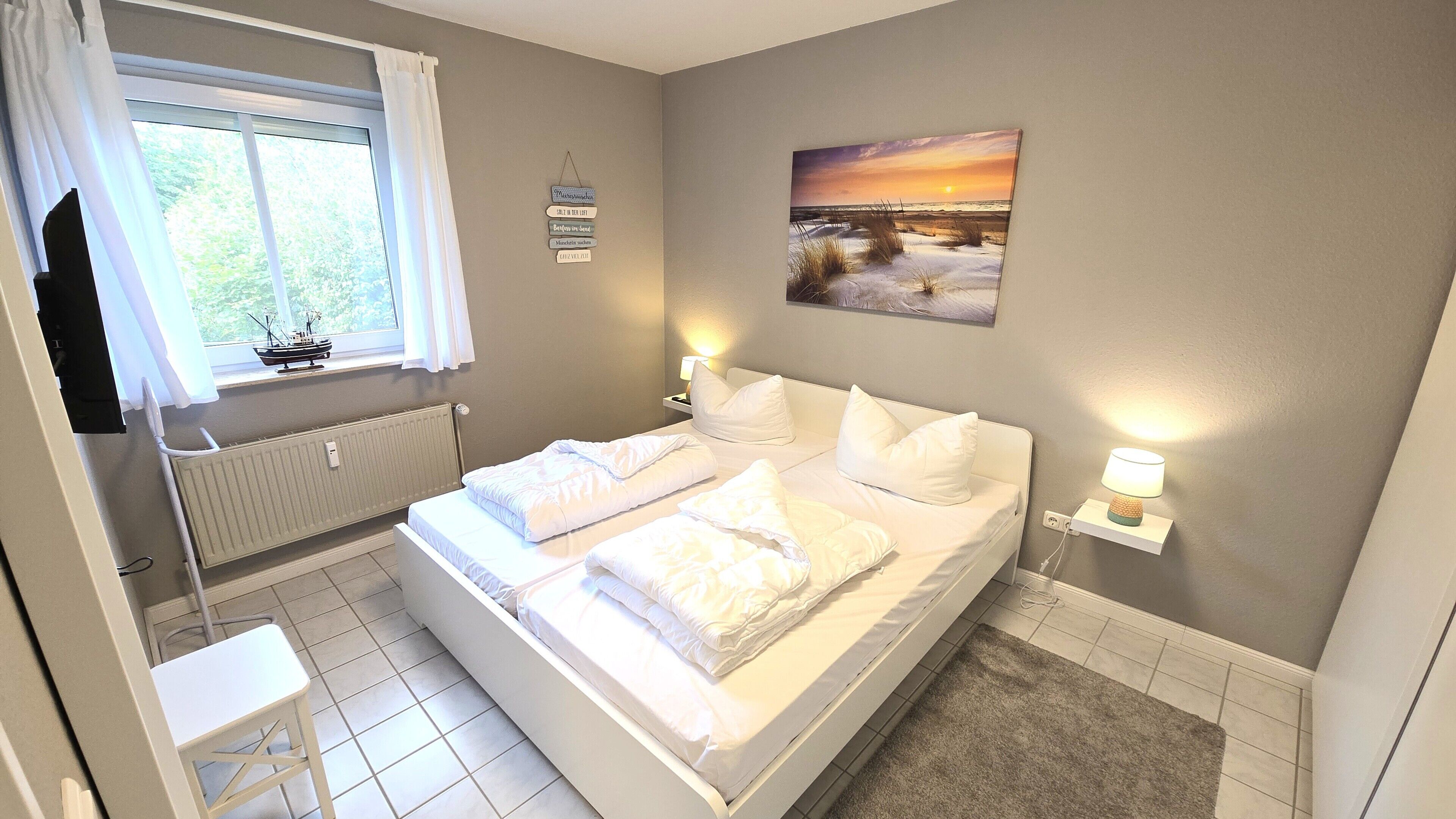 Ein Hotelzimmer mit einem Bett, einem Fenster mit Vorhängen, einem Wandbild, einem Nachttisch mit einer Lampe und einer Heizung.