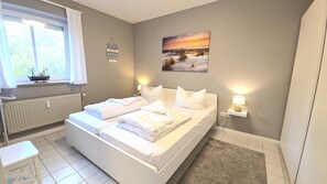 A bedroom with a bed, bedside lamps, a window, a radiator, and a small table. - Fantastic vacation rental "FeWo Lieblingsplatz" right on the beach in California O (Schönberg (Holstein))