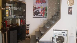 A kitchen with a bar area, a poster of Naruto, a clock, and a washing machine.