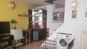 A compact living space with a TV, a small bar area, a washing machine, and a poster of Naruto.