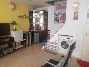 A compact living space with a TV, a small bar area, a washing machine, and a poster of Naruto.