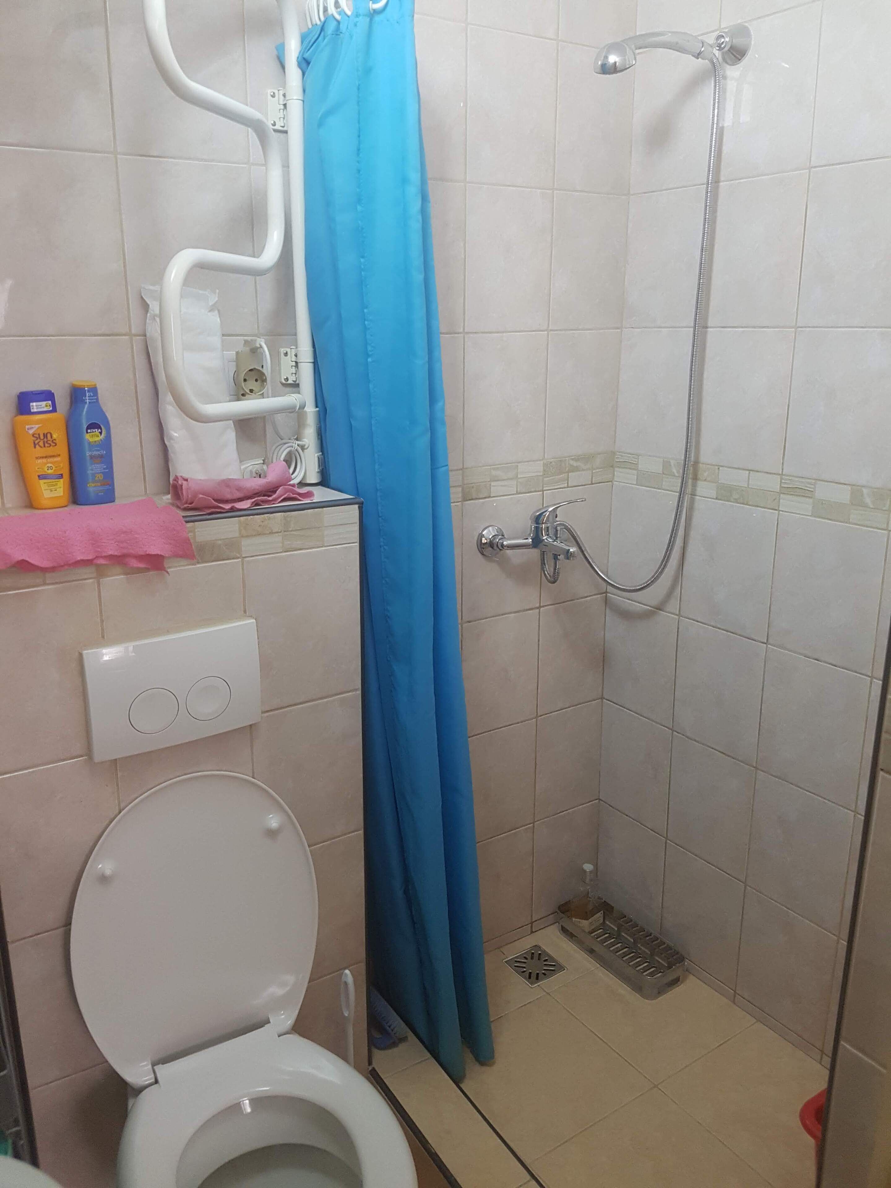 Ein Badezimmer mit weißer Toilette, einer Dusche mit blauer Duschkabine und einem gefliesten Boden.