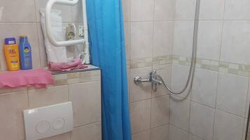 Ein Badezimmer mit weißer Toilette, einer Dusche mit blauer Duschkabine und einem gefliesten Boden.