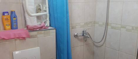 A bathroom with a white toilet, a shower with a blue curtain, and a tiled floor.