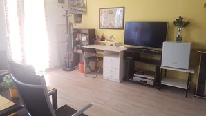 A room with a desk, chair, television, and a small cabinet.