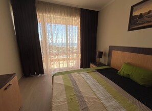 Een hotelkamer met een bed, nachtkastje, lamp en een schilderij aan de muur.