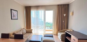 Habitación de hotel con sofá, una mesita, escritorio y balcón con cortinas.