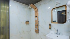 A modern bathroom with a marble wall, a shower with a curved design, a sink with a mirror, and toiletries on the wall.