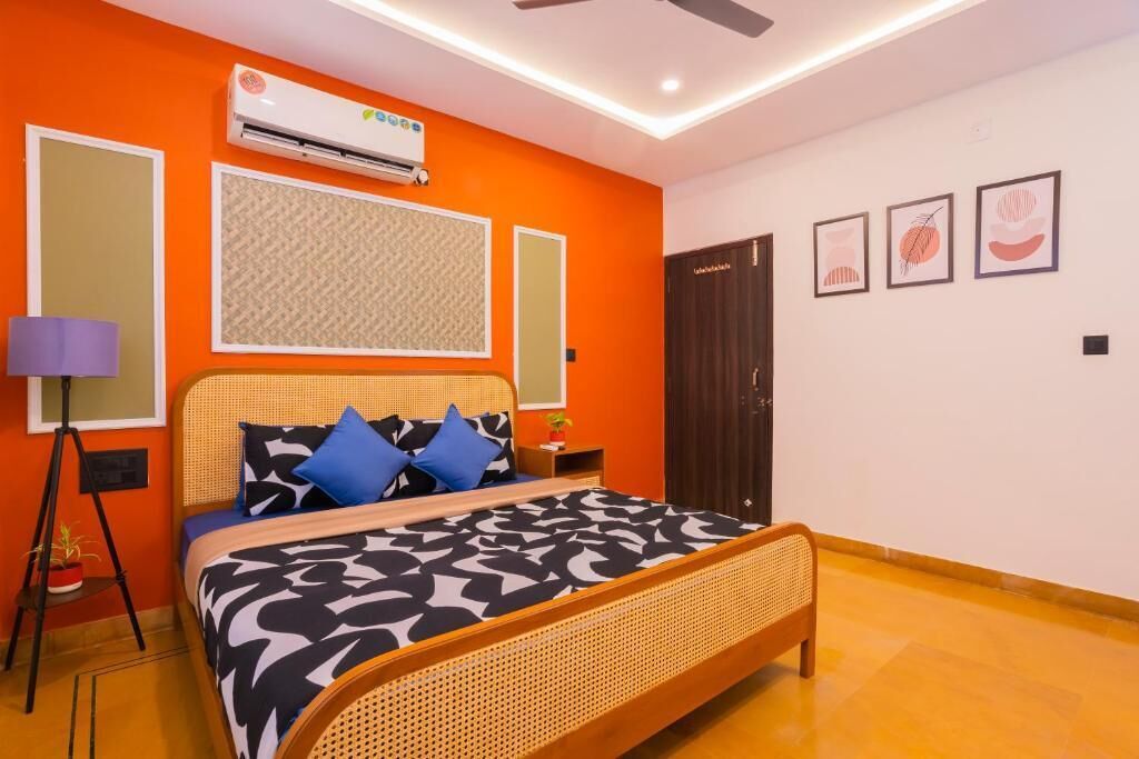 A bedroom with a bed, a standing lamp, an air conditioner, and framed artwork on the wall.