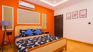 A bedroom with a bed, a standing lamp, an air conditioner, and framed artwork on the wall.