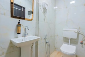 Un baño con lavamanos blanco, espejo, cabezal de ducha manual y retrete.