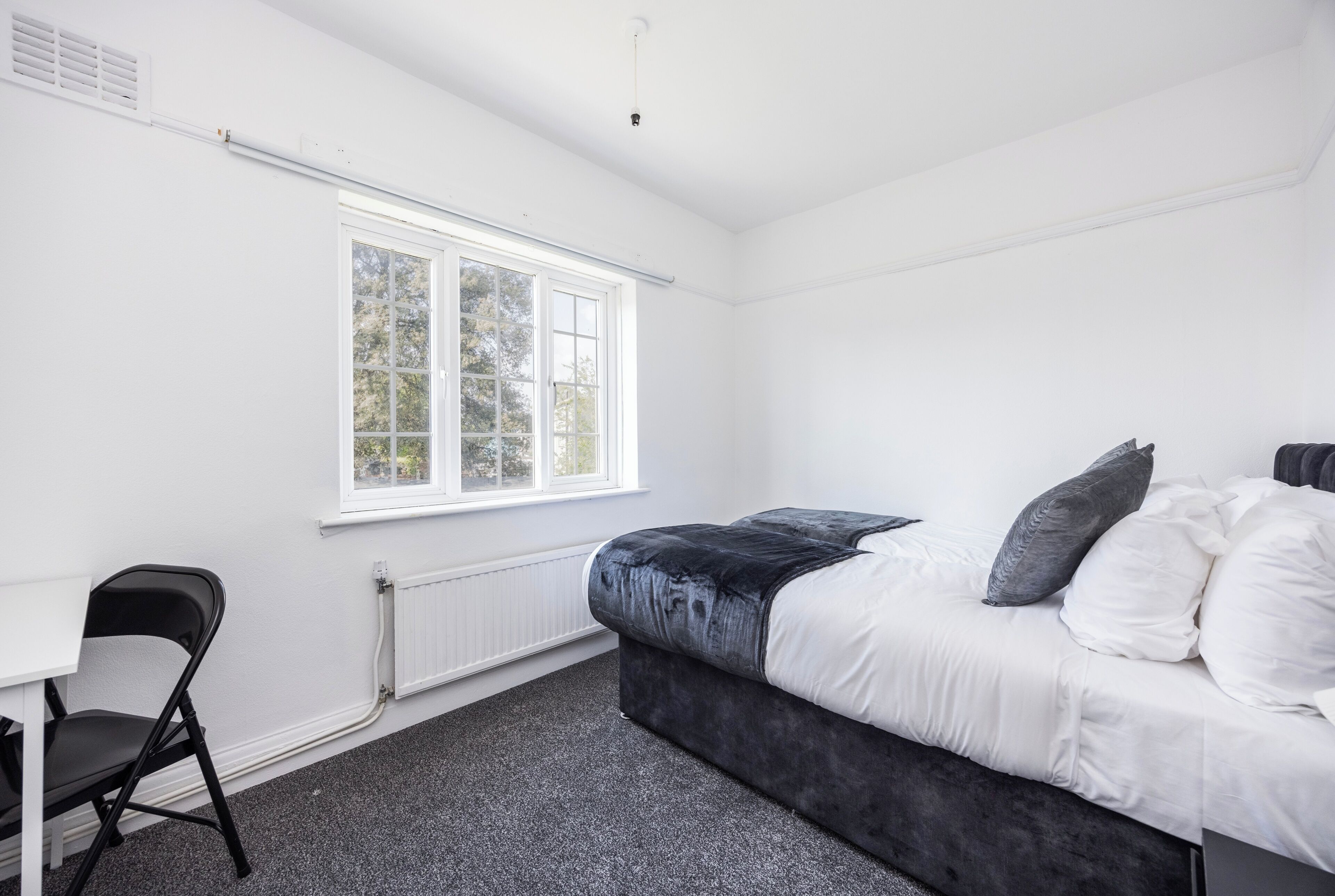 Un dormitorio con cama, una silla, una ventana y un radiador.