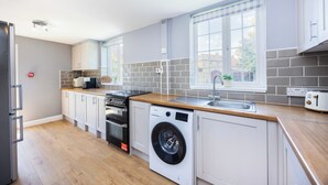 Una cocina moderna con horno empotrado, lavavajillas y lavadora, encimera de madera y ventana con vistas al exterior.