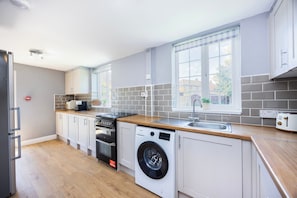 Eine moderne Küche mit Einbauofen, Geschirrspüler und Waschmaschine, einer Holz Arbeitsplatte und einem Fenster mit Blick hinaus.