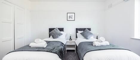 Habitación de hotel con dos camas individuales, una mesita de noche pequeña con lámpara y un cuadro en la pared.