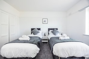 A hotel room with two single beds, a small bedside table with a lamp, and a framed picture on the wall. - 8 Bed - Sleeps 14 - Large Garden - Parking 10 Cars (Tilbury)