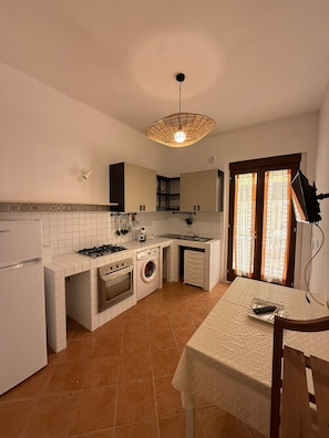 Une cuisine compacte équipée d’une cuisinière à gaz, d’un four, d’un lave-linge et d’un coin repas avec une table et des chaises.