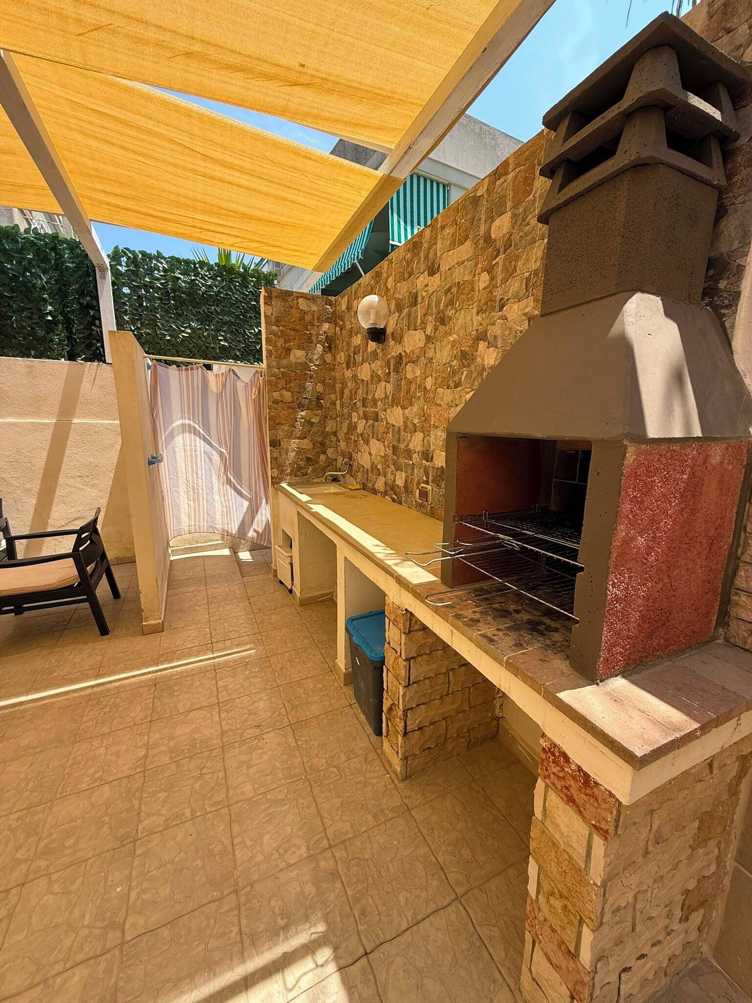 An outdoor kitchen area with a stone wall, a grill, and a table with chairs.