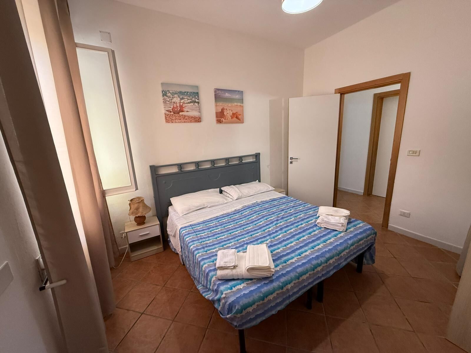 Een slaapkamer met een bed, een nachtkastje, een lamp en twee schilderijen aan de muur.