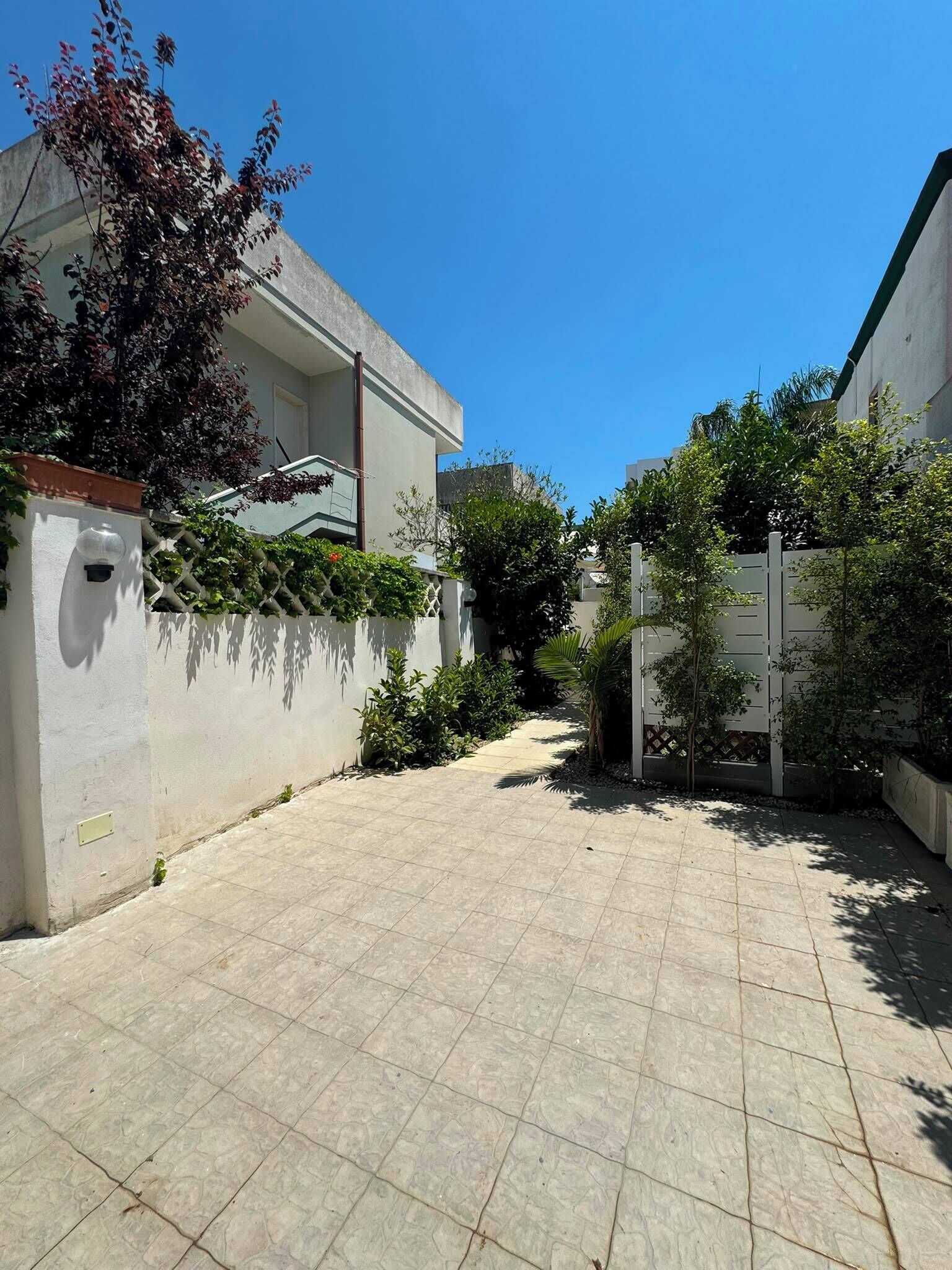 A courtyard with a tiled floor, a white wall with a security camera, and a tree with red leaves.
