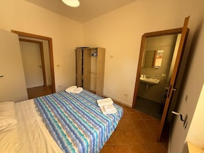 Quarto com cama, guarda-roupa e banheiro com pia.