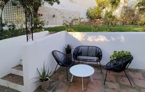 Eine Terrasse mit einem weißen Tisch und zwei Stühlen, umgeben von Blumentöpfen und einer weißen Wand.