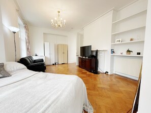 A spacious room with a large bed, a television, a wardrobe, and a radiator. - Stylish Retreat at Hyde Park Mansions (London)