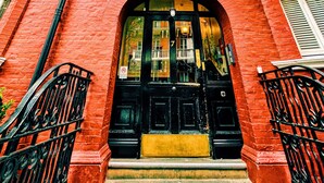 Ein Gebäude aus roten Ziegeln mit schwarzem Eingang, verzierten Fensterrahmen und einem Balkon mit schwarzen Geländern.