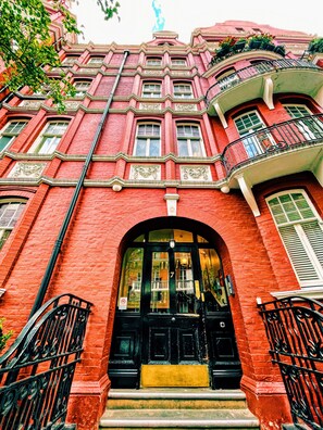 A red brick building with a black entrance, ornate window frames, and a balcony with black railings. - Stylish Retreat at Hyde Park Mansions (London)