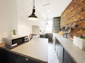 A kitchen with a granite countertop, a built-in oven, a sink, and a hanging pot rack. - Stylish Retreat at Hyde Park Mansions (London)