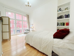 A bedroom with a bed, a bookshelf, a window with a view of buildings, and a chandelier. - Stylish Retreat at Hyde Park Mansions (London)