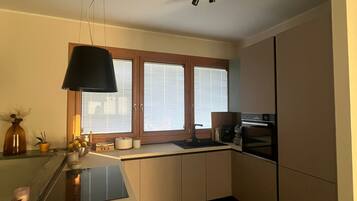 A modern kitchen with a central island, built-in appliances, and a window with blinds.