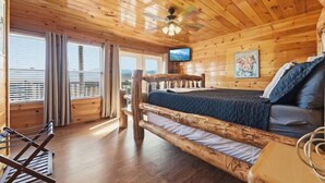 A wooden cabin room with a bed, a television, and a window with blinds. - Robin's View | Hot Tub, Indoor Pool, Unbeatable Mountain Views! (Pigeon Forge)