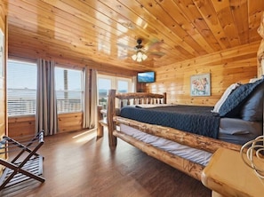 A wooden cabin room with a bed, a television, and a window with blinds. - Robin's View | Hot Tub, Indoor Pool, Unbeatable Mountain Views! (Pigeon Forge)