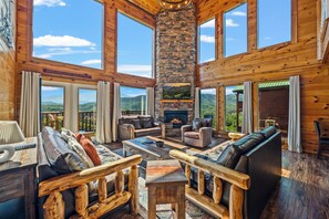 A spacious log cabin interior with a fireplace, multiple seating areas, and large windows offering scenic mountain views. - Robin's View | Hot Tub, Indoor Pool, Unbeatable Mountain Views! (Pigeon Forge)