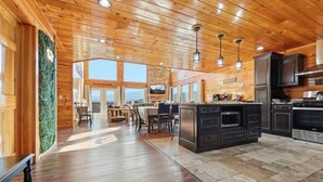 A spacious kitchen with wooden ceiling and cabinetry, a dining area with a large window, and a stone-tiled floor. - Robin's View | Hot Tub, Indoor Pool, Unbeatable Mountain Views! (Pigeon Forge)