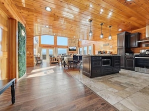A spacious kitchen with wooden ceiling and cabinetry, a dining area with a large window, and a stone-tiled floor. - Robin's View | Hot Tub, Indoor Pool, Unbeatable Mountain Views! (Pigeon Forge)