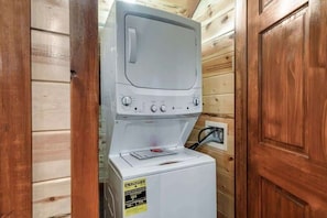 A white washing machine with a control panel, placed in a wooden room with a door.