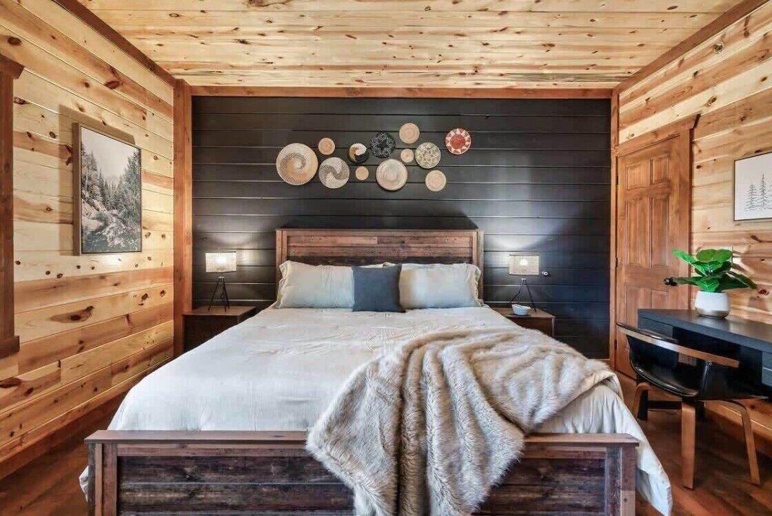 A wooden cabin bedroom with a bed, bedside tables, a wall-mounted clock, and a framed picture.