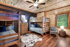 A cabin interior with bunk beds, a wooden ceiling, a ceiling fan, a cowhide rug, and a window with blinds.