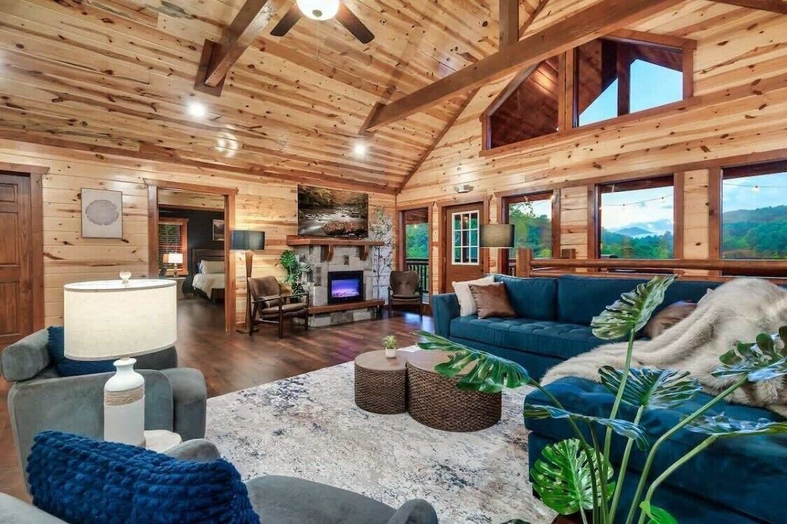 A spacious living room with a fireplace, comfortable seating, and large windows offering a view of the outdoors.